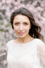 Naklejka premium portrait of a cute and beautiful caucasian woman girl in a dress in the garden in the middle of blooming sakura. spring and sun time. Blurred background and selected focus.