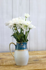 Fresh white flowers in green milk jug on light wooden background close up