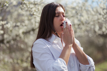 Young woman sneezing in the blossoming garden
