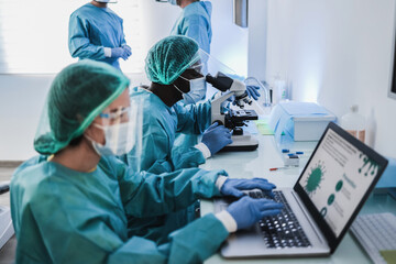 Medical workers in hazmat suit working with microscope and laptop computer inside modern laboratory...