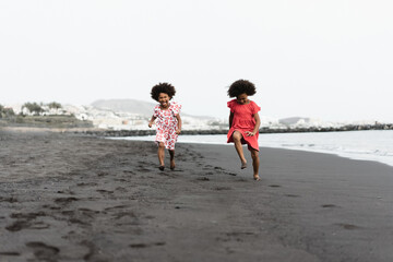 Happy african sister twins running on the beach together during summer time - Main focus on left...