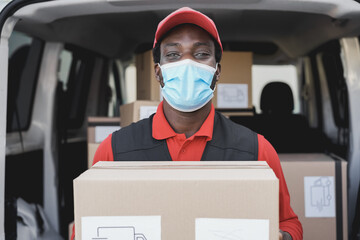 African delivery man smiling on camera while wearing safety mask - Focus on face