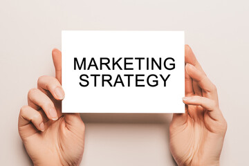 Female hands hold card paper with text Marketing Strategy on a yellow background. Business and finance concept