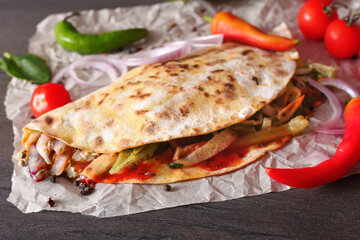 Spicy Mexican tacos on craft paper with pepper, onion and tomatoes on a dark wooden surface top view with place for text. Food delivery
