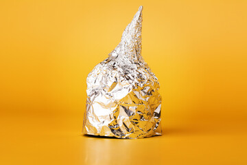Hat made of aluminium foil on yellow background.