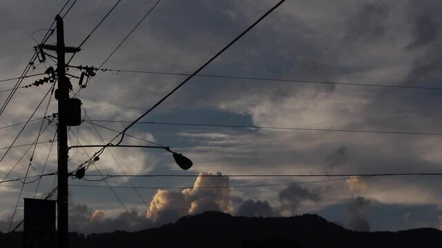 Silhouette of telephone line and moving clouds in background. Low angle and static shot