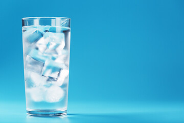 A glass with ice and clean water on a blue background.