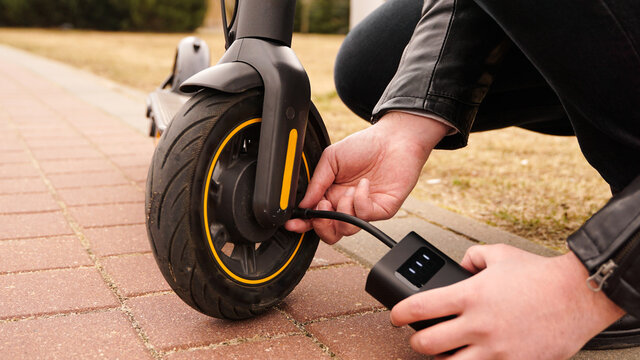 A man pumps air into the wheel of an electric scooter using a special device.