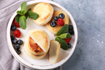 Healthy breakfast. Cheesecakes, cottage cheese pancakes with honey, fresh berries, mint on a white wooden plate on a gray table. Background image, copy space, horizontal