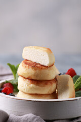 Healthy breakfast. Cheesecakes, cottage cheese pancakes with honey, fresh berries, mint on a white wooden plate on a gray table. Background image, copy space, vertical