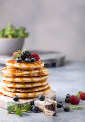 Pancakes with honey and fresh berries, mint on a white wooden board on a gray table. Background image, copy space, vertical