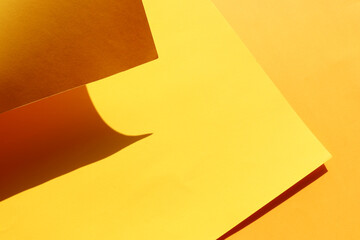 Folded yellow paper. Shape, hard light, shadows. Abstract styled orange background with lines and curve. Copy space