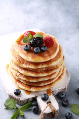 Pancakes with honey and fresh berries, mint on a white wooden board on a gray table. Background image, copy space, vertical