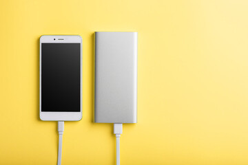 Smartphone charging with power bank by wire on yellow background.