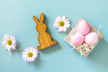 Minimal spring Easter concept. Paper box with Easter eggs in pink tones and chrysanthemums flower on pastel blue background. Top view flat lay.