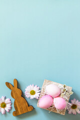 Paper box with Easter eggs in pink tones and spring chrysanthemums flower on pastel blue background. Minimal Easter concept. Top view flat lay. Copy space.