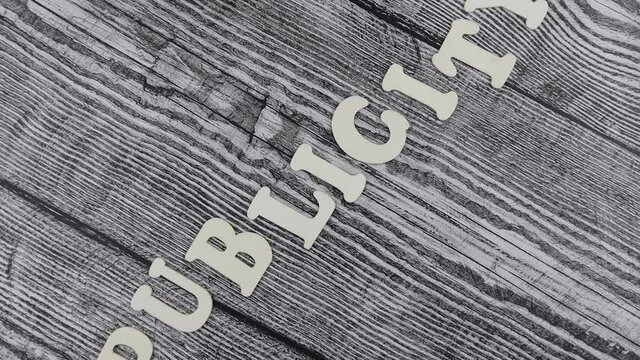 Publicity - concept with descending alphabet letters on cubes in a wavy line over old rustic wooden plank background. Rotation
