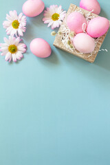 Minimal spring Easter concept. Paper box with Easter eggs in pink tones and chrysanthemums flower on pastel blue background. Top view flat lay. Copy space.