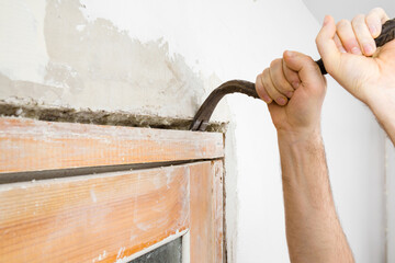 Young adult man hands using crowbar and breaking old wooden door frame from wall. Closeup....
