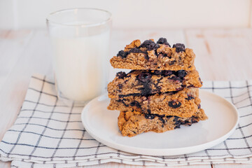 Stack of homemade oatmeal scones with berries stacked on white plate and glass of plant based milk. Vegan sweet baked food. Gluten free pastry. Healthy breakfast.