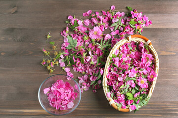 fragrant rose petals and flowers scattered on a dark wooden table. glass bowl and wicker basket with pink flowers. top view, space for text