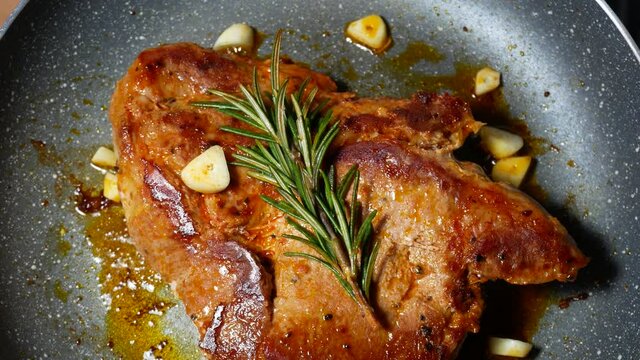 Delicious juicy pork steak seasoned with rosemary and garlic is fried in a pan.