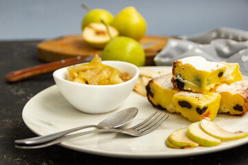 Sliced pie on a white plate with pear jam on a black table. Green pears in the background are blurred. Morning breakfast