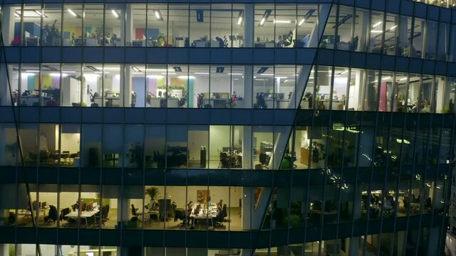 A view from a drone on the windows of offices in a skyscraper building at night. close-up 4k resolution. Drone shot at a skyscraper with offices and people working with computers in the offices 
