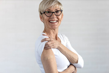 Proud mature woman smile after vaccination with bandage on arm