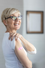 Proud mature woman smile after vaccination with bandage on arm