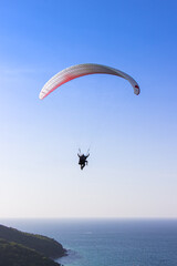 Paraglider flying over lush green mountains from view point on Koh Larn island in Pattaya, Chonburi Thailand.