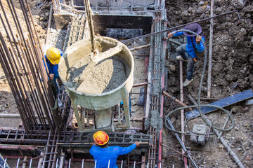 Worker pouring cement pouring into foundations formwork at building area in construction site.