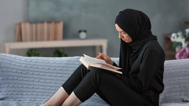 Focused Arabic woman in traditional black hijab reading book relaxing on couch. 4k Dragon RED camera