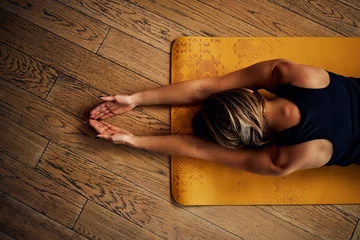 Poster Im Rahmen Top view of a woman practicing yoga at home. © chika_milan