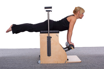 A 50-year-old trainer practices Pilates on an elevator chair, lying on her stomach supporting...
