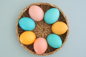 Easter composition of Easter colorful eggs in pastel colors of yellow, blue and pink in a wicker basket on a gentle blue background, top view, flat lay