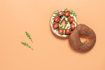 Fresh bagel sandwich with cream cheese, cherry tomato and arugula. Pastel peach background. Top view, flat lay.