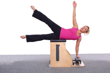 A 50-year-old trainer practices Pilates on an elevator chair by lying on her side and supporting herself with one arm while the other is up