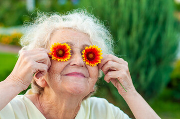 Mature woman 60 plus is lying on the lawn holding chamomile eyes. Care for women's wrinkled skin....