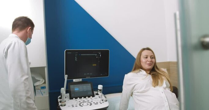 A young pregnant girl came to see a doctor. Doctor doing 3d ultrasound on belly in clinic. Process of fetal ultrasonography