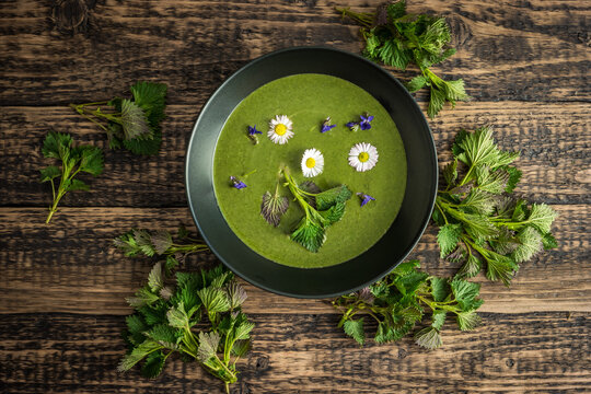 Healthy green spring nettle soup with edible flowers garnished with nettle leaves served on Green Thursday