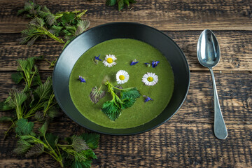 Healthy green spring nettle soup with edible flowers garnished with nettle leaves and spoon served on Green Thursday