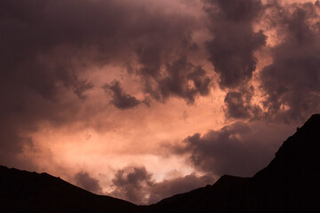 Cloudscape. Dramatic sky with colorful clouds and the mountains dark silhouette at sunset. 