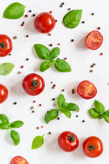 Bright juicy pattern made with cherry tomatoes, fresh basil leaves and peppercorn on white marble background. Vertical image. Healthy food concept.