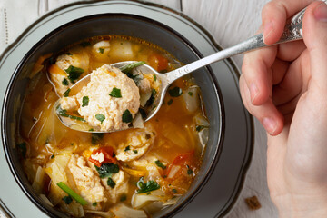 Hand of a young girl holds in the spoon a chicken meatball during eating a soup
