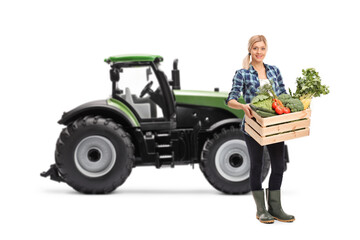 Female farmer with a crate full of organic vegetables standing in front of a tractor