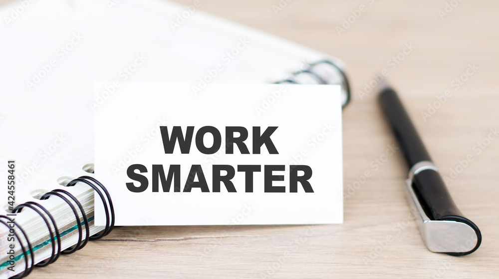 Poster card with text work smarter next to a notebook and a black pen on the table