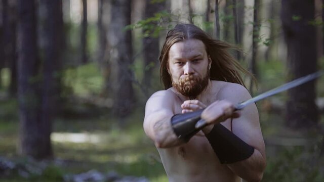 Practice with edged weapons in the forest. The guy has a knife and he stabs looking in the direction of the camera