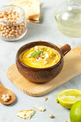 Hummus in a brown ceramic bowl on a gray table with butter in a jug, chickpeas and lime. Close-up, vertical frame