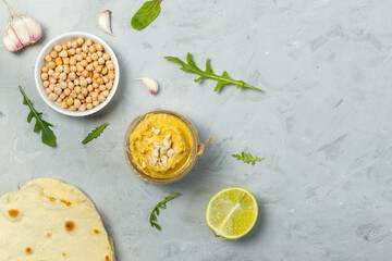 Fototapeta na wymiar serve hummus in a small glass jar on a gray surface with tortilla, chickpeas, garlic and lime. Top view, with space